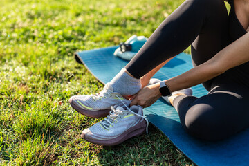 Young sporty women in sportswear sitting on yoga mat and tie shoelaces after doing yoga training and workout in the park while exercise for healthy wellness lifestyle with outside nature
