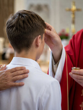 Priest anointing young boy during confirmation sacrament in catholic church. Religious ceremony with prayer and blessing. Christian rite of passage faith education and spirituality.