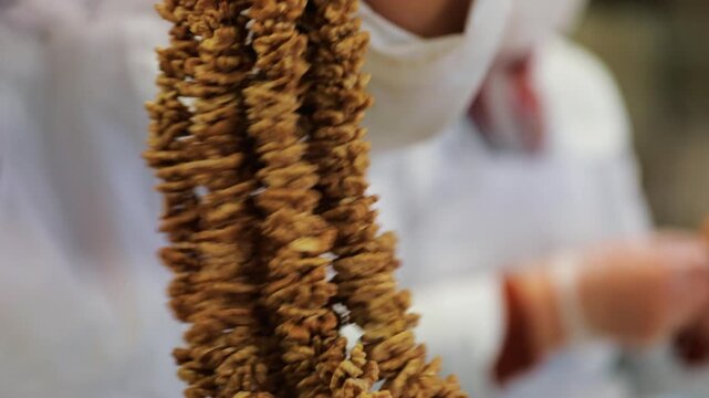Preparation stage of traditional Turkish walnut sausage (cevizli sucuk); hanging walnut strings on a wooden rod for production. Regional food processing and handmade culinary concept.