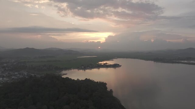 Sunset over Lak Lake in Lien Son Lak Commune, Dak Lak Province, Vietnam, featuring traditional wooden boats on the lake and peaceful rice fields surrounded by the Central Highlands landscape.