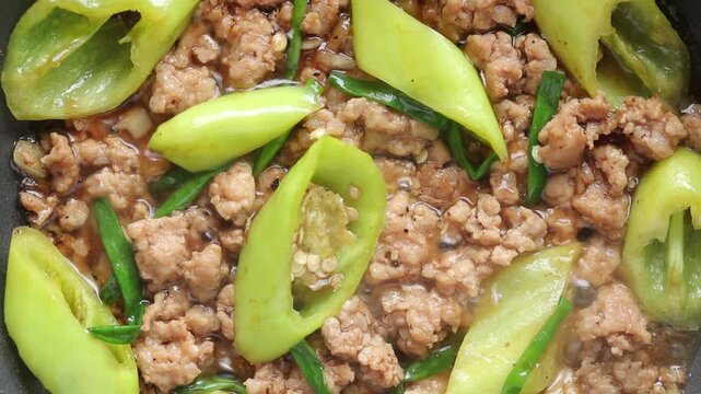 Top view of stir-fried green chili peppers with minced pork cooking in a hot pan.