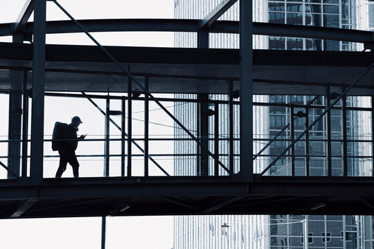 A pedestrian silhouette crosses a steel and glass bridge walkway in Oslo, Norway, where the Barcode grid frames the business district