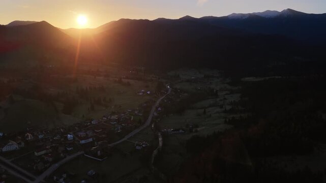 Aerial drone view down a valley with a road and scattered houses, surrounded by forest, characteristic of Dorna Arini, Romania, near Acoperamantul Maicii Domnului Monastery