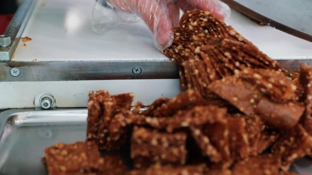 Cutting of sesame and grape molasses fruit leather (pestil) in a food production facility. Mass production and packaging process of traditional Anatolian snacks.
