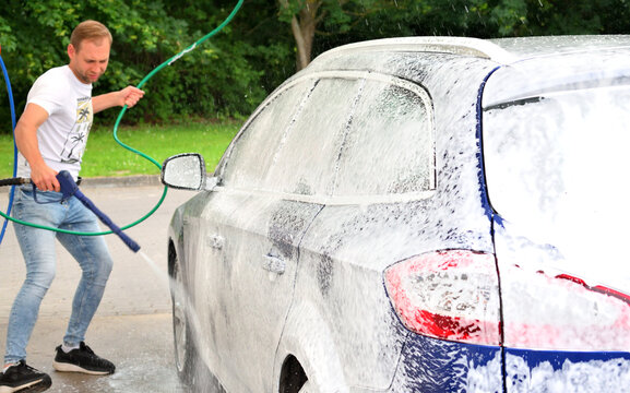 Man applying active snow foam layer to a car body at a self-service car wash station