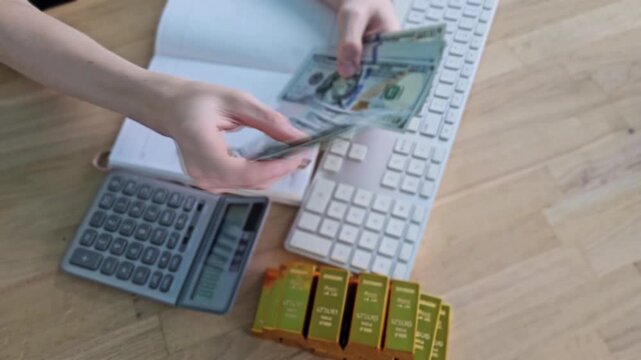Counting cash and managing gold bars in an office setting with a calculator and notebook