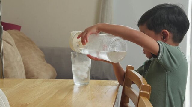 Close up of child pouring water into glass with Ice for refreshment