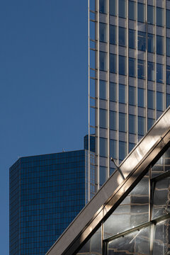 A glass skyscraper facade rises beside a bridge under blue sky, where windows and reflection sharpen the urban geometry of the high-rise edge