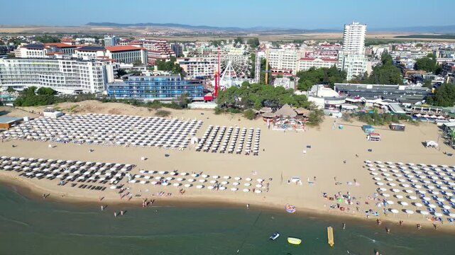 Rows of beach umbrellas and a ferris wheel at Sunny Beach in Bulgaria during a sideways flight along the coastline. A drone captures the Black Sea shore.