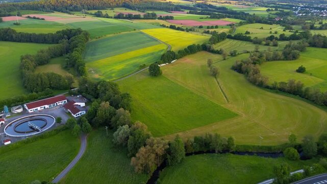 Aerial drone view of patchwork farmland, rapeseed fields and wastewater treatment facility in rural Germany during summer