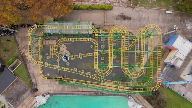 Roller coaster train moves along winding yellow track in outdoor amusement park setting