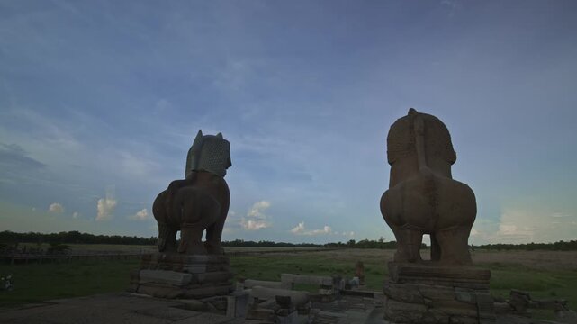 Aincient Angkorian sandstone lion statues overlook baray lake filled with grass at the start of rainy season. Motion control dynamic movement time lapse.