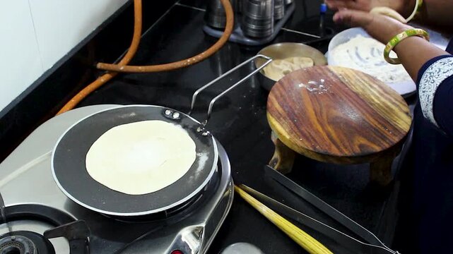 Woman simultaneously rolling dough on chakla with belan while chapati cooks on tawa. Perfect for Indian cooking shows, food documentaries, and domestic lifestyle content.