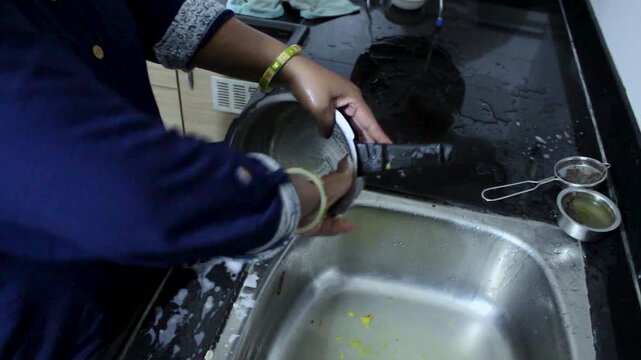 Woman rinsing large steel pressure cooker over sink after cooking. Perfect for domestic chores, South Asian household lifestyle, kitchen hygiene, and real-life family content.