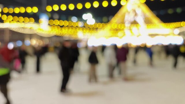 People ice skating at winter rink with festive lights blurred background.