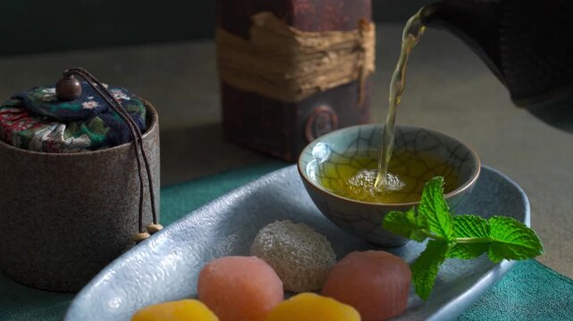 Green tea is pouring into ceramic cup alongside traditional Japanese mochi.