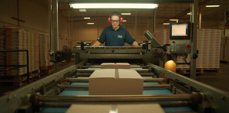 Factory operator monitoring a packaging machine and conveyor belt in a logistics warehouse with operator packaging conveyor warehouse logistics industrial production manufacturing