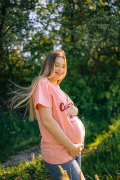 Pregnant woman smiling outdoors in nature, happy expecting mother holding baby bump in sunlight