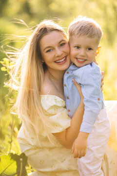Young mother hugging her smiling toddler son outdoors in a sunlit summer meadow