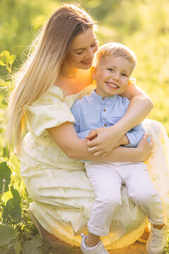 Mother hugging smiling son in a sunlit meadow &mdash; family love and outdoor summer portrait