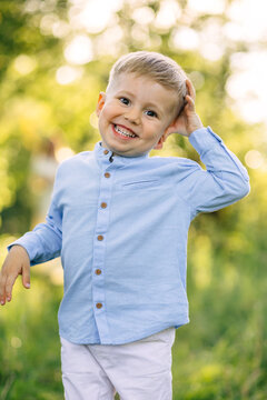 Happy little boy smiling in blue shirt playing outdoors in a sunlit green park