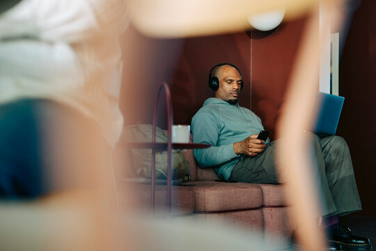 Businessman doing multi-tasking with laptop and phone while sitting on couch at coworking space