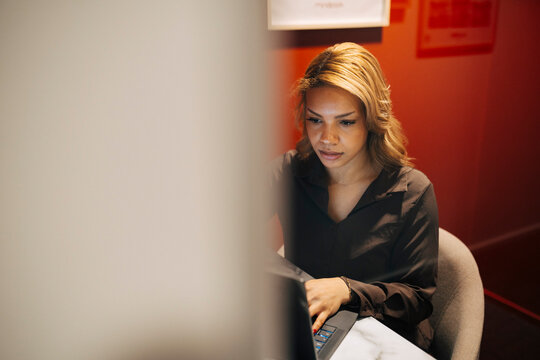Businesswoman with highlighted hair working on laptop while sitting at coworking space