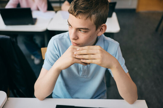 High angle view of thoughtful schoolboy looking away while sitting at desk in classroom
