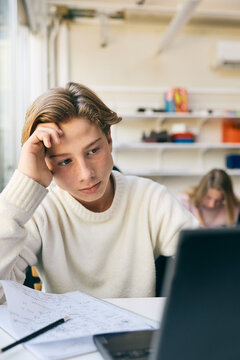 Stressed teenage schoolboy solving math problems while using laptop in classroom