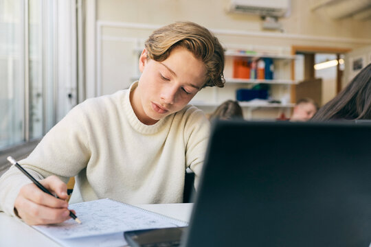 Focused teenage schoolboy solving math problem while sitting at desk in classroom