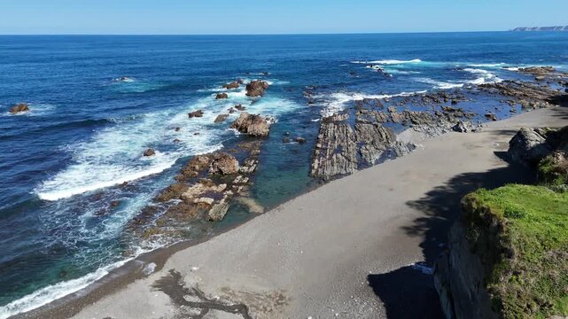 Aerial tilt up reveal shot of a wild pebble beach and unique rocky formations in the turquoise sea under a clear sky