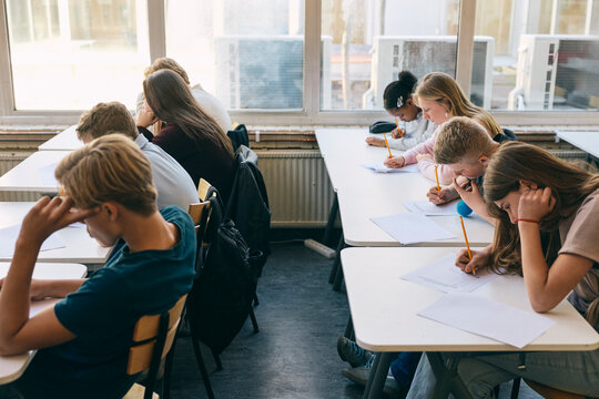 Teenage boys and girls writing educational exam while sitting at desk in junior high classroom