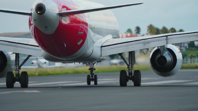 Low angle close up of red and white regional turboprop aircraft on airport runway showing landing gear, wheel, wing underside and turboprop engine
