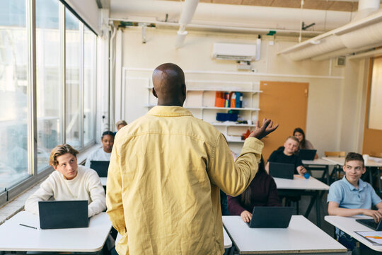 Rear view of male professor teaching students in classroom at junior high school