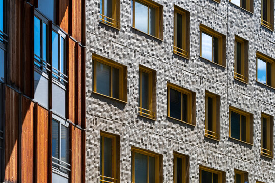 In La Confluence, Lyon, France, an apartment facade sets wood beside stone, with windows and pattern forming quiet geometry across the wall