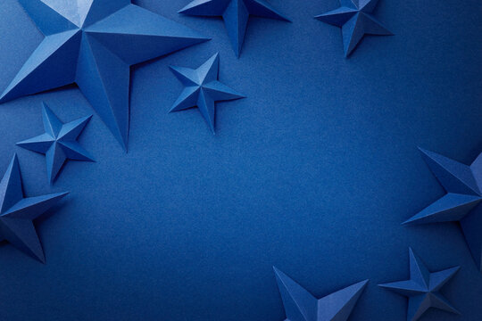 Monochrome blue composition with folded paper stars arranged around the edges on a dark blue background. Patriotic border with empty space for text, suitable for Independence, Fourth of July, Memorial