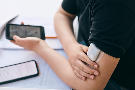 Midsection of schoolboy with wearing glucose monitor on arm while sitting at desk in classroom