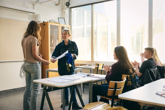 Happy teacher giving certificate to female student in classroom at school