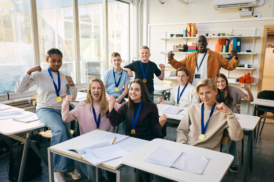 Portrait of junior high students wearing medals showing winning fist with teacher in classroom at school
