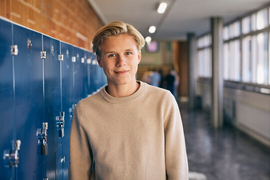 Portrait of smiling teenage boy standing near lockers in junior high school lobby