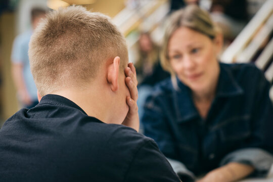 Emotional stressed boy getting consoled by female teacher in school