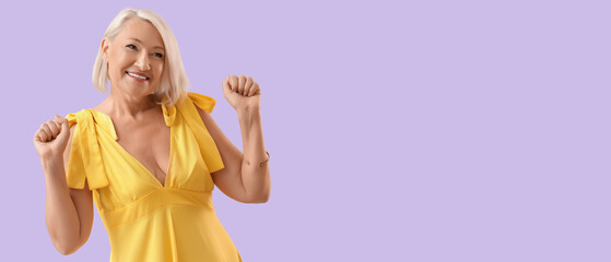 Obraz premium Beautiful mature woman in yellow dress dancing on lilac background
