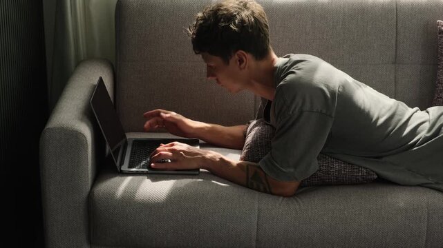 Remote worker using couch as improvised workspace adapting home environment for laptop work and flexible modern lifestyle