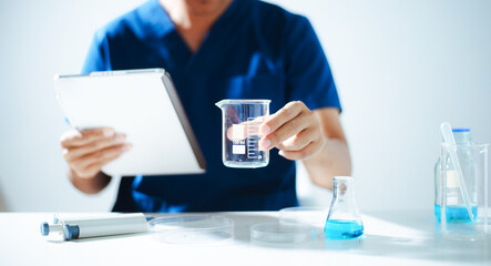 Fototapeta premium A professional scientist in a lab coat inspecting blue and white medical capsules on a petri dish. Concept of pharmaceutical research, health care development