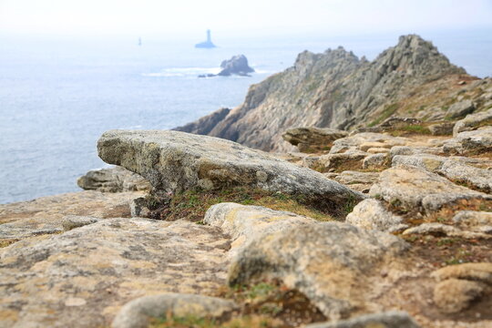 Raue Felsklippen fallen steil in den Atlantik ab, w&auml;hrend im Hintergrund die ber&uuml;hmten Leuchtt&uuml;rme Phare de la Vieille und T&eacute;vennec aus den unruhigen Wellen ragen.