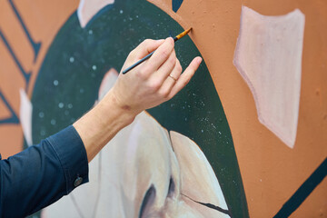 Close up view of artist hand painting detailed wall mural with fine brushstrokes © TRAVELARIUM