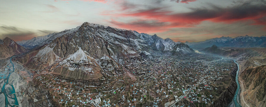 Aerial view of the Booni settlement in a mountain valley with snow-capped peaks and a winding river under a sunset sky in Chitral, Khyber Pakhtunkhwa, Pakistan.