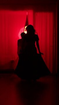 Silhouette of Indian couple dancers performing graceful duet in front of sheer red curtain