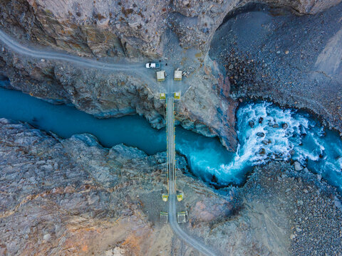 Aerial view of a narrow bridge crossing a turquoise river flowing through a deep rocky canyon with a winding mountain road Chitral, Khyber Pakhtunkhwa, Pakistan.