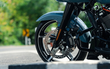 Obraz premium Close up of motorcycle front wheel with disc brake, parked on road with blurred greenery in background